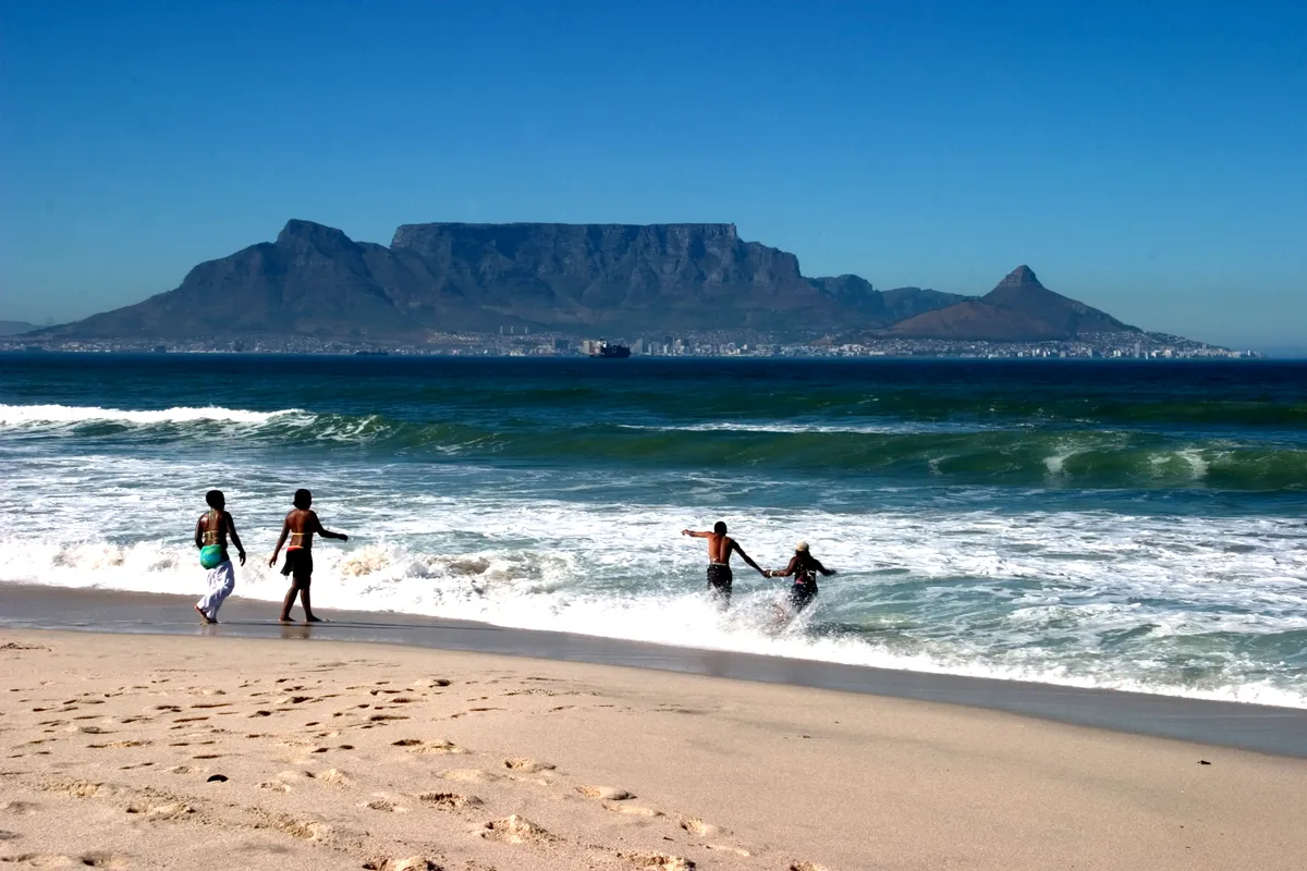 Surfers running into the waves at Bloubergstrand with Table Mountain behind