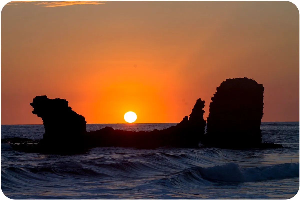 The sun setting behind the El Tunco rock on the beach at La Libertad