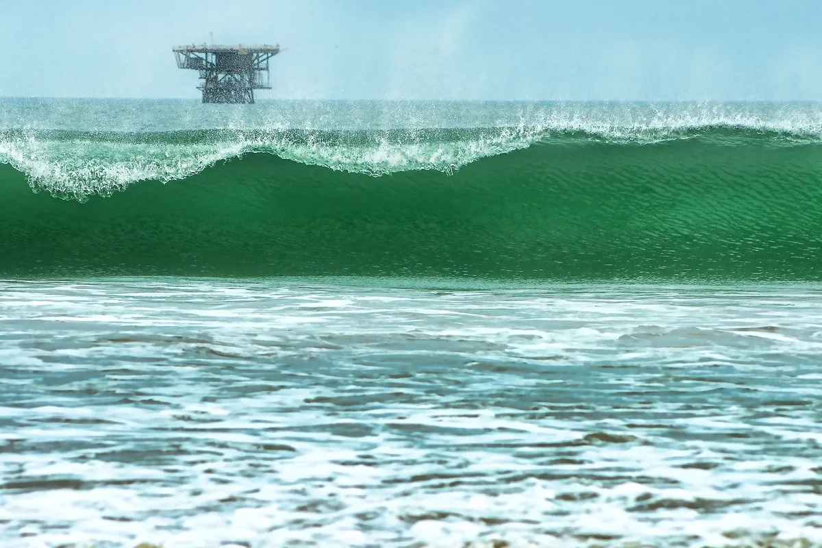 A green wave breaking at Lobitos with an offshore oil platform behind