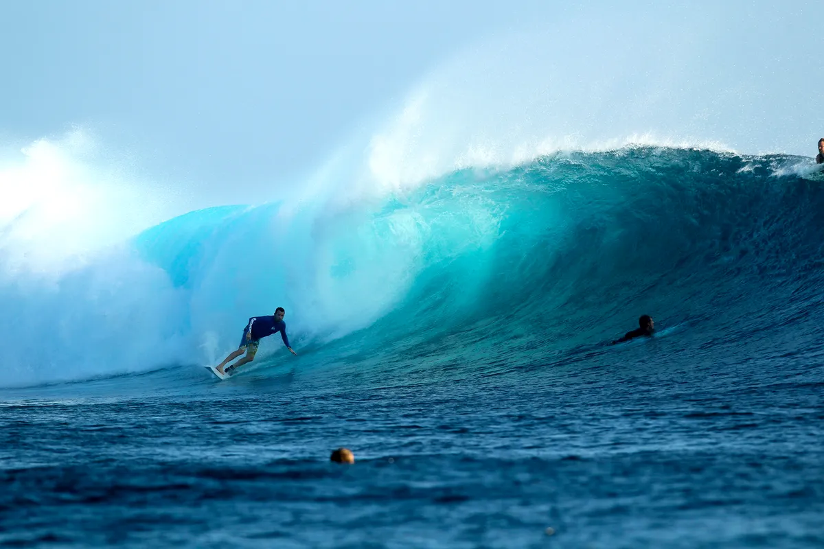 A surfer dropping into a blue wall at Cloudbreak, Fiji