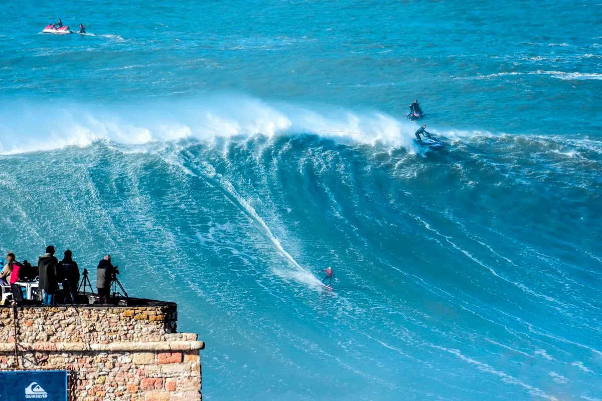 A surfer on a giant wave at Praia do Norte as spectators watch from the Nazaré headland