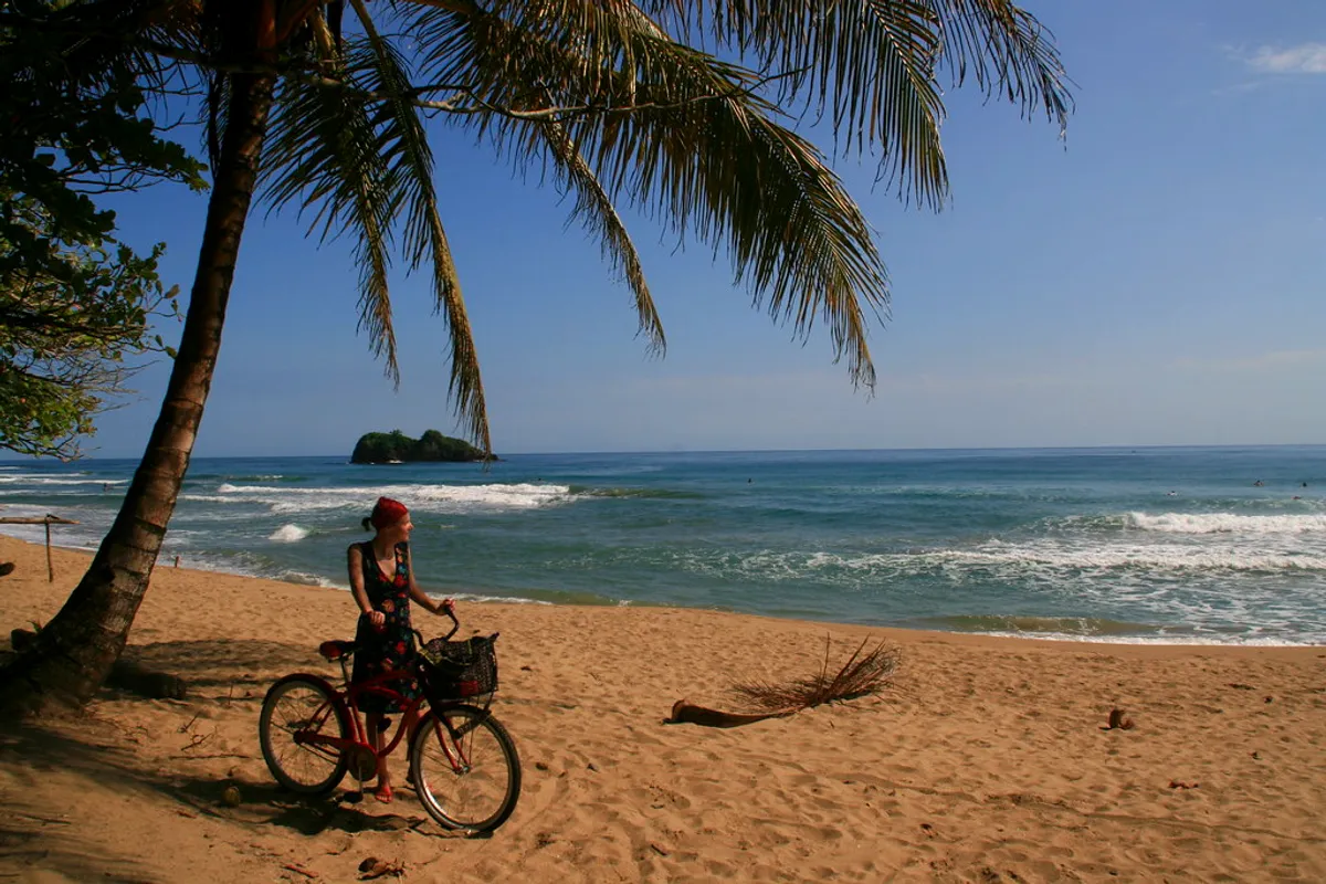 A cyclist under palm trees on the sand at Playa Cocles near Puerto Viejo