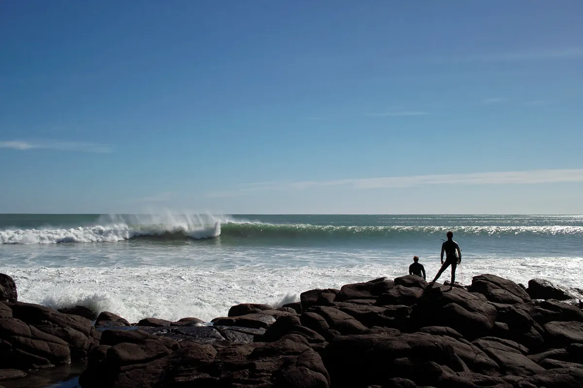 A surfer on the rocks watching lines of swell wrap into Manu Bay, Raglan