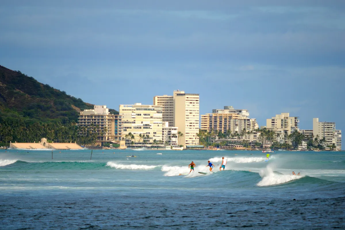 Surfers on gentle waves at Waikiki with hotels and Diamond Head behind
