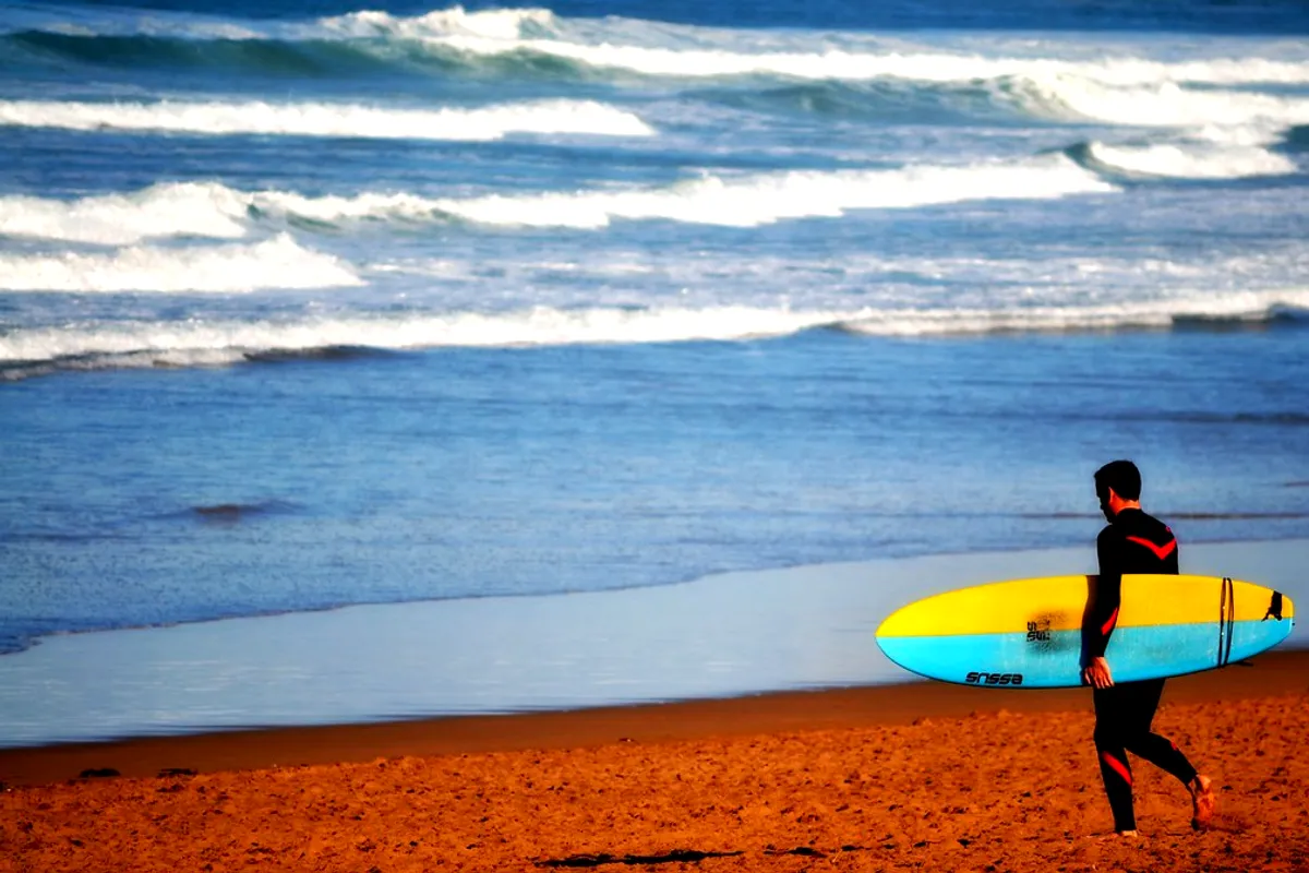 A surfer carrying a yellow board along the waterline at Zarautz